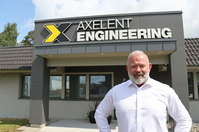man i vit skjorta står framför entré med texten Axelent Engineering